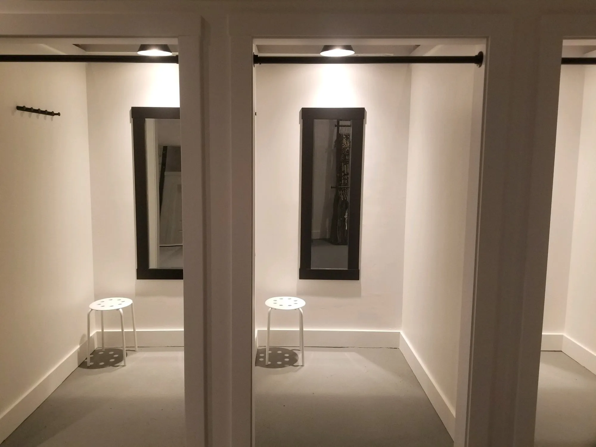 Two finished retail fitting rooms with framed mirrors and stools