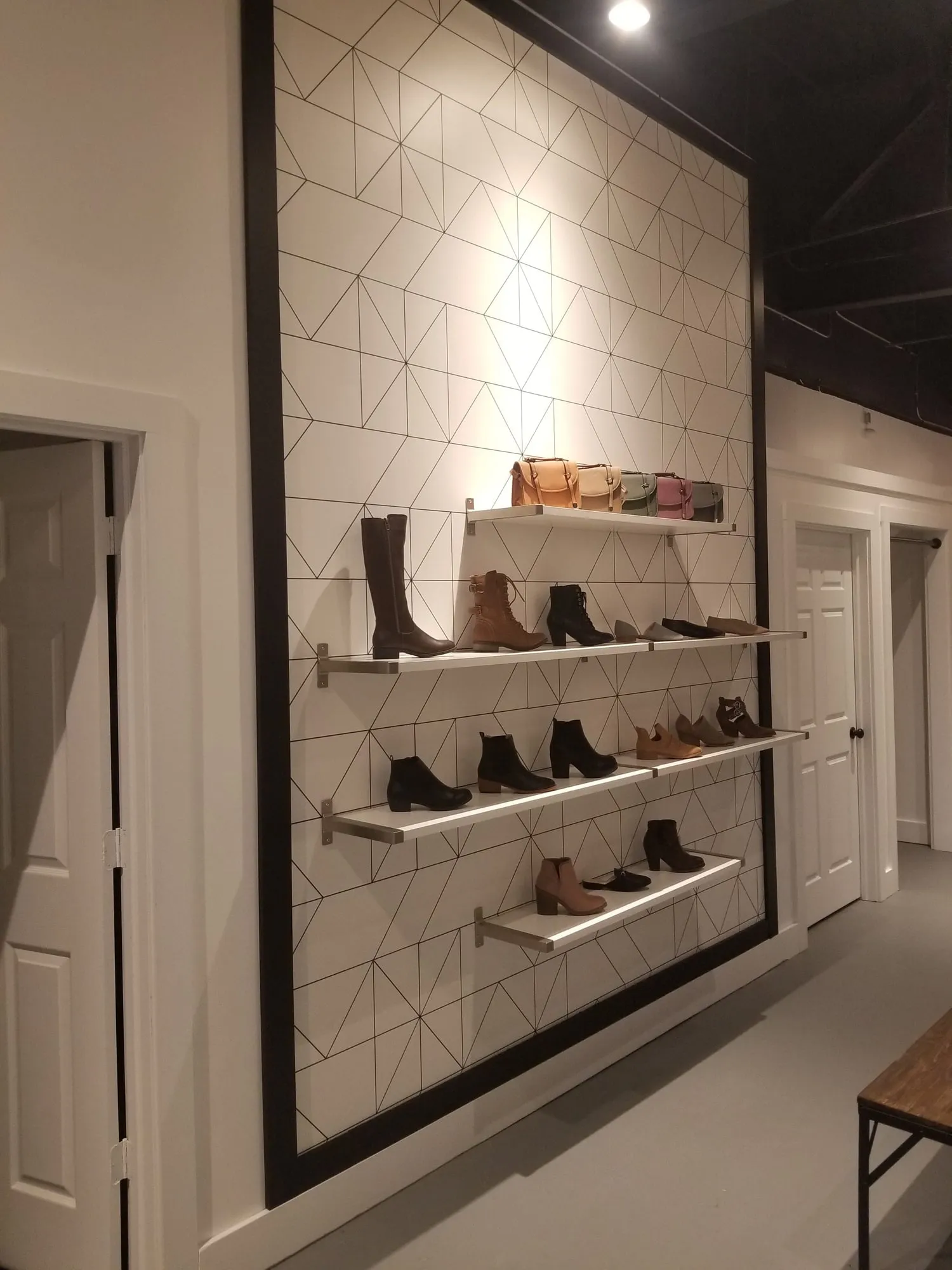 Retail display wall with white geometric tile and floating shelves of footwear