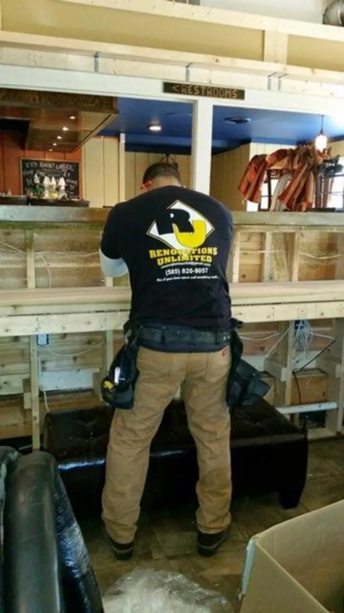 A Renovations Unlimited crew member in a company shirt framing a new bar