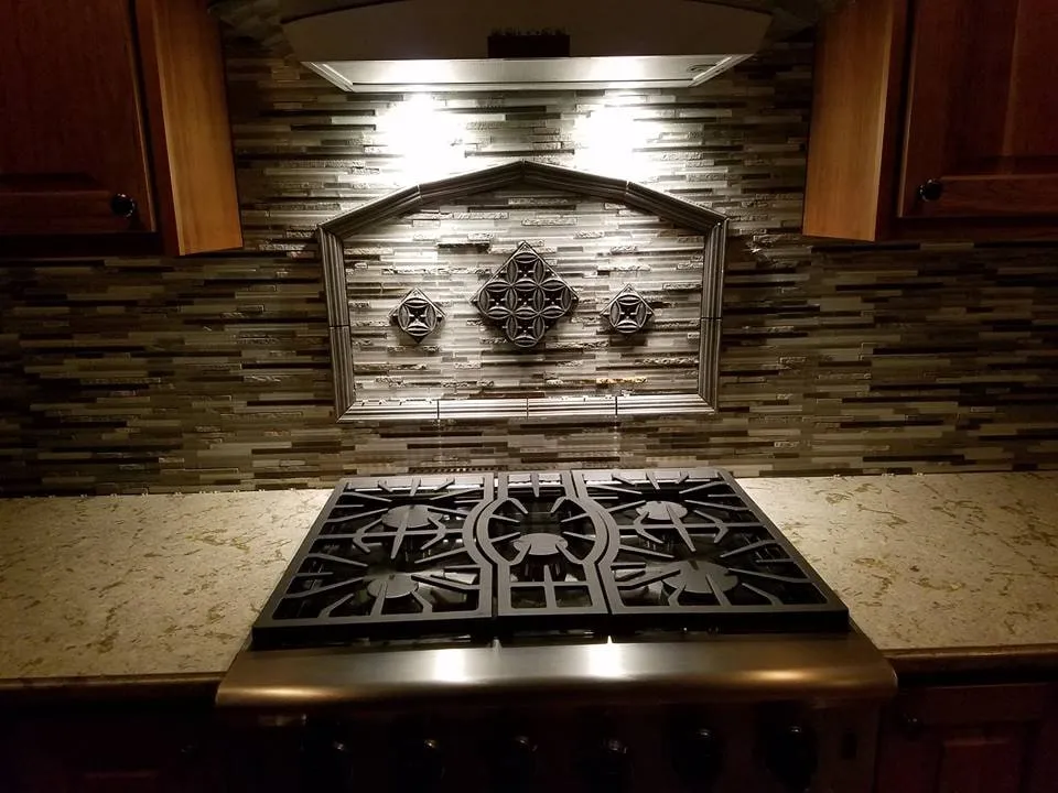 Gas cooktop set into granite below a dark glass mosaic backsplash with a decorative tile medallion
