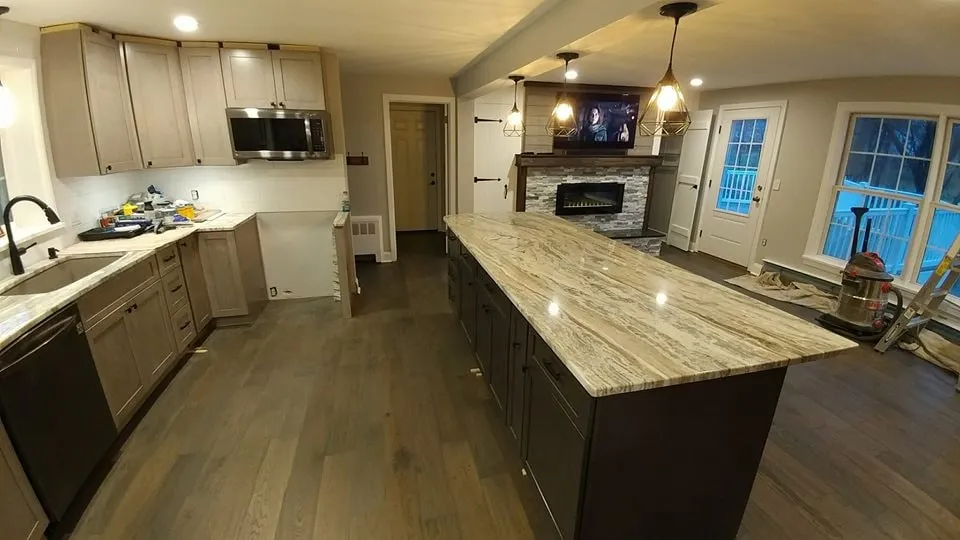 Open-plan kitchen with a long quartz island, dark cabinetry and wide-plank wood flooring