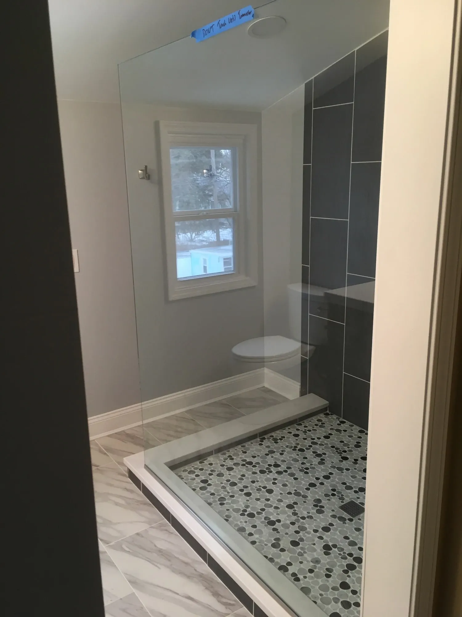 Completed walk-in shower with large-format gray tile and a pebble mosaic floor