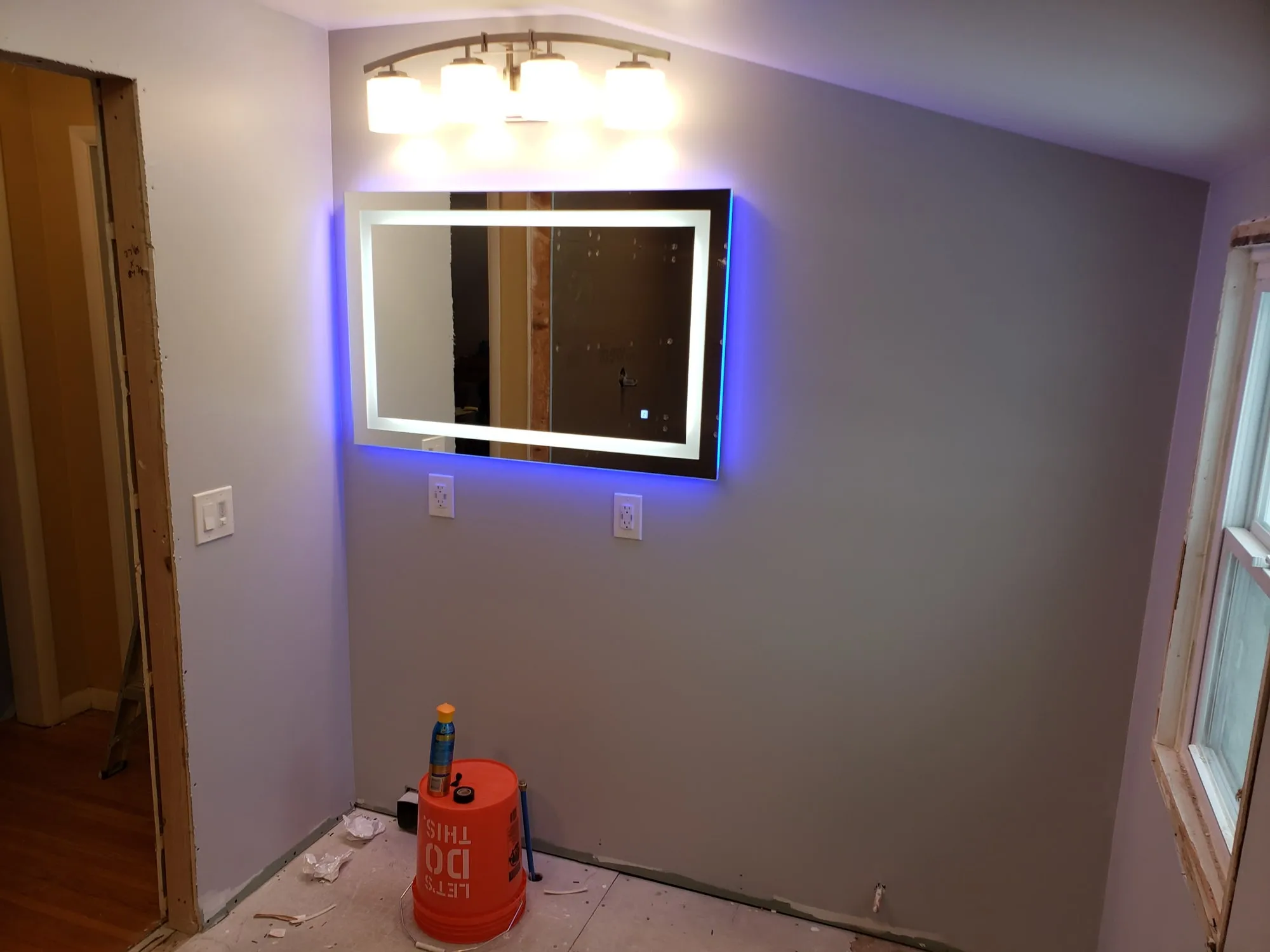 Backlit LED mirror mounted on a gray painted bathroom wall