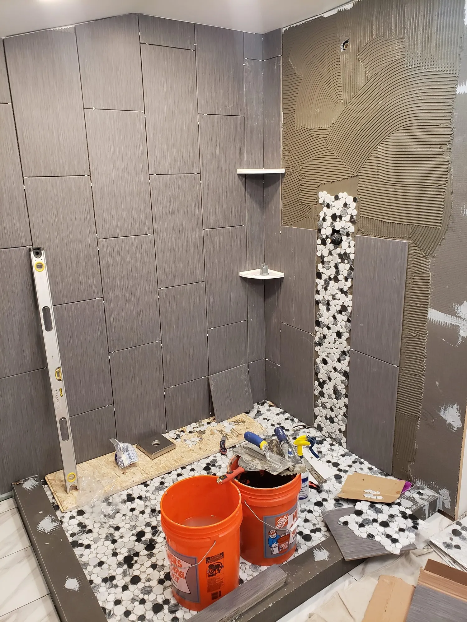 Pebble mosaic shower floor set against large-format wall tile