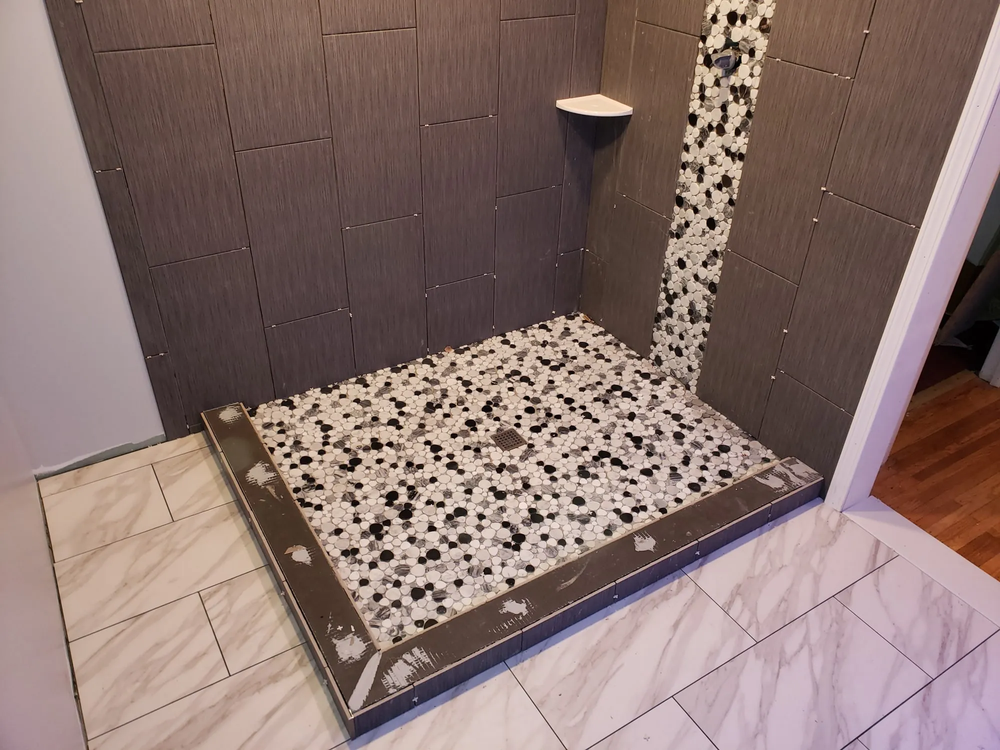 Shower niche and pebble accent strip tiled into a gray tile surround